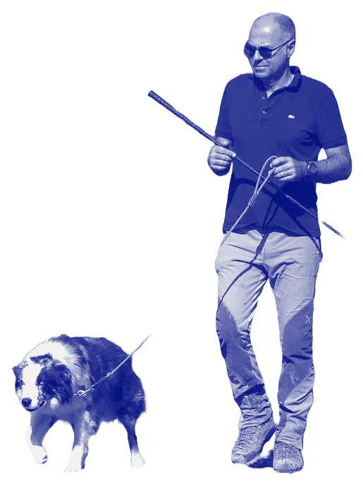 Giovanni cammina all’aperto con gli occhiali da sole, accanto a un border collie al guinzaglio.
