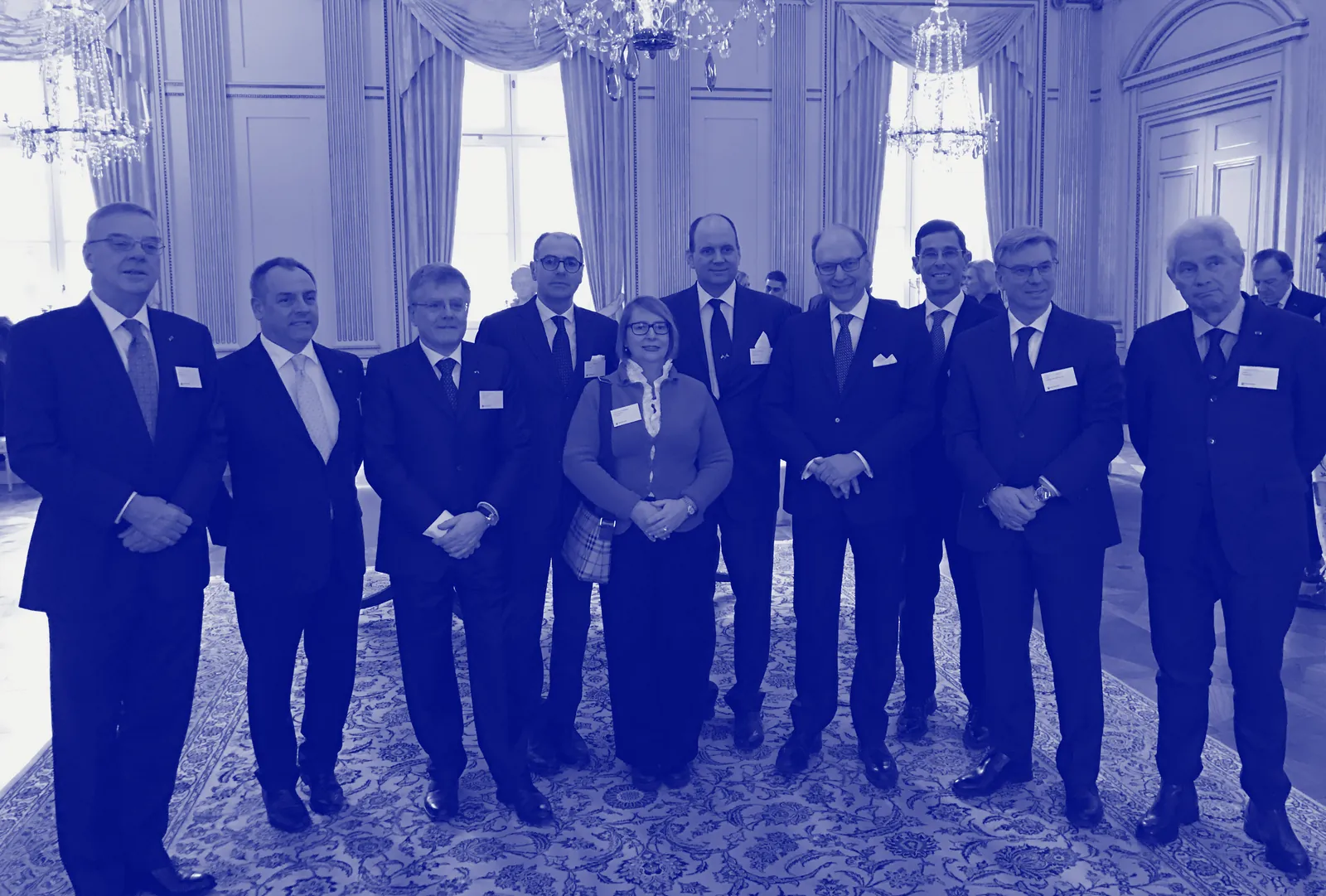 Foto di gruppo in un salone con lampadari di cristallo; Giovanni è il quarto da sinistra.