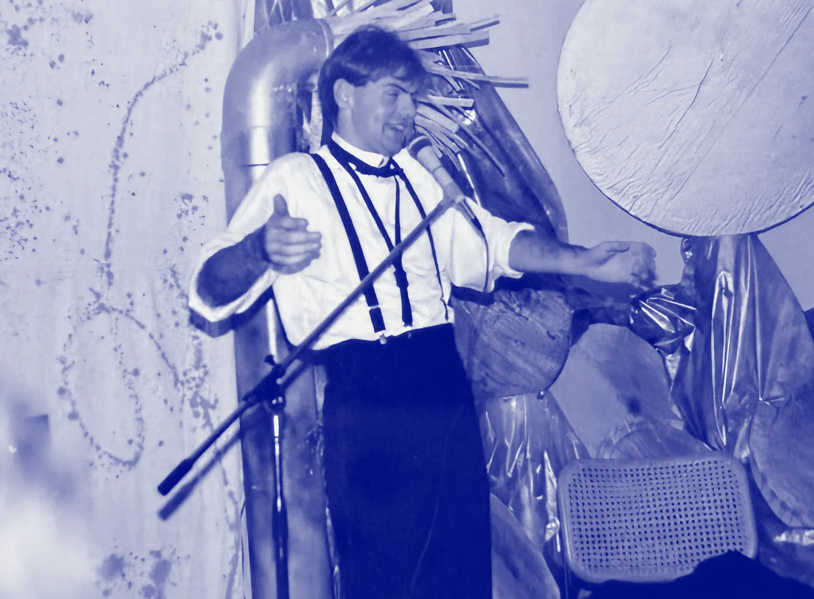 Giovanni da giovane su un palco, camicia bianca e bretelle, parla al microfono con le braccia aperte.